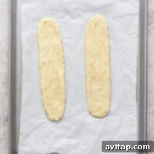 Two unbaked dough logs placed on a parchment-lined baking sheet, ready to be baked.