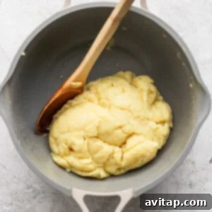A wooden spoon rests in a pot containing a cooked dough mixture.