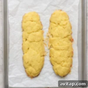 Two homemade almond biscotti cookie logs on a parchment-lined baking sheet.
