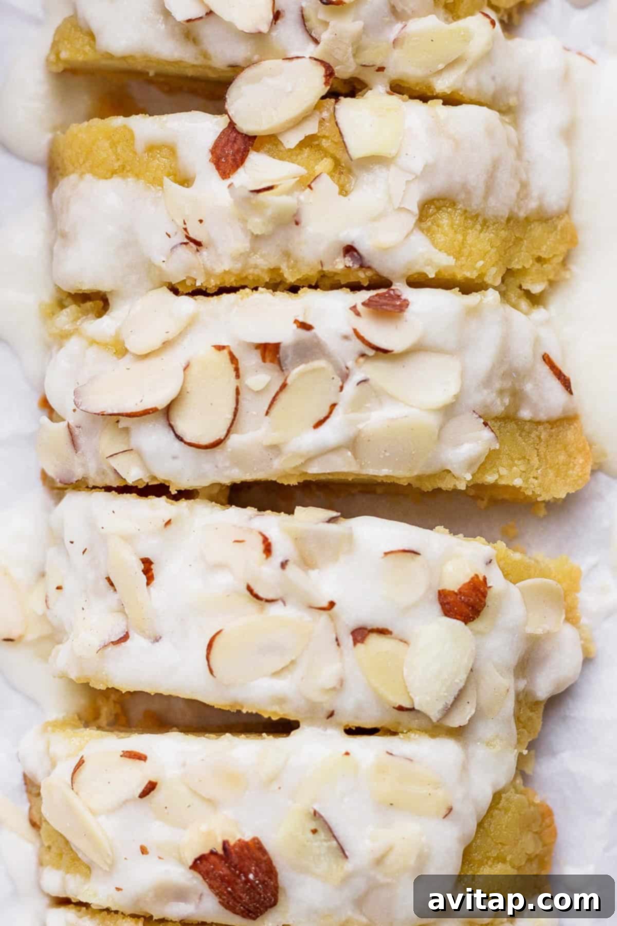 Sliced almond cake topped with white icing and sprinkled with almond slivers.