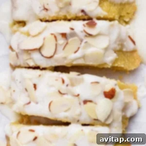 Close-up of almond-topped biscotti with a white icing drizzle. The biscotti pieces are stacked closely together, showcasing the almond slices and the glossy icing.