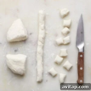 Dough is cut into small pieces on a white cutting board with a wooden-handled knife beside them.