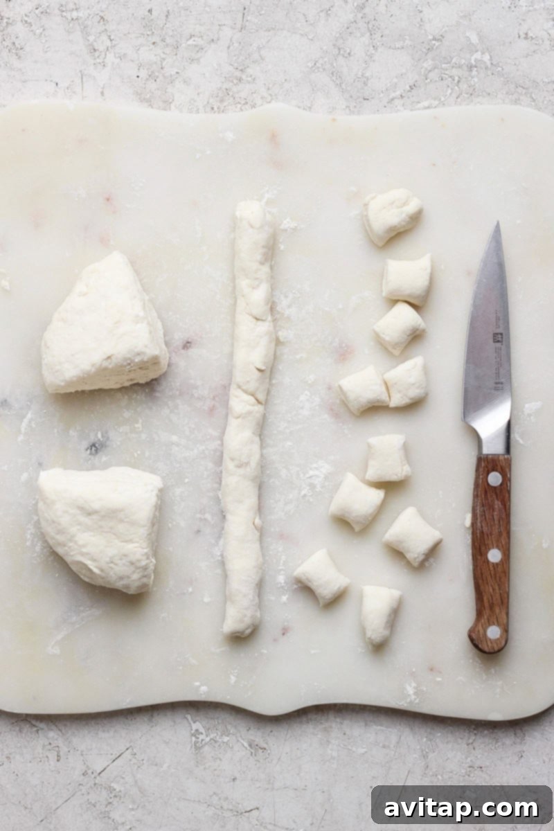 Dough being prepared on a cutting board with a knife. Dough is rolled into a log and cut into small pieces.