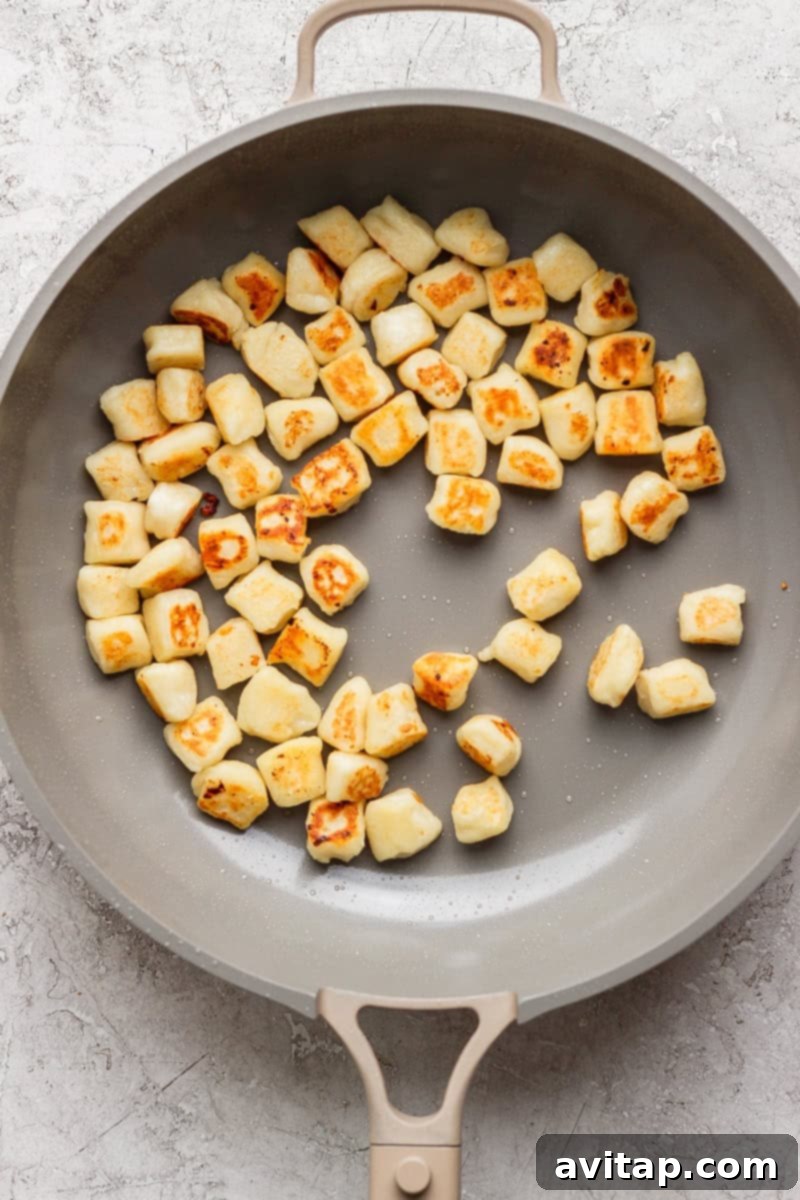 Pan with evenly browned gnocchi pieces on a light surface.
