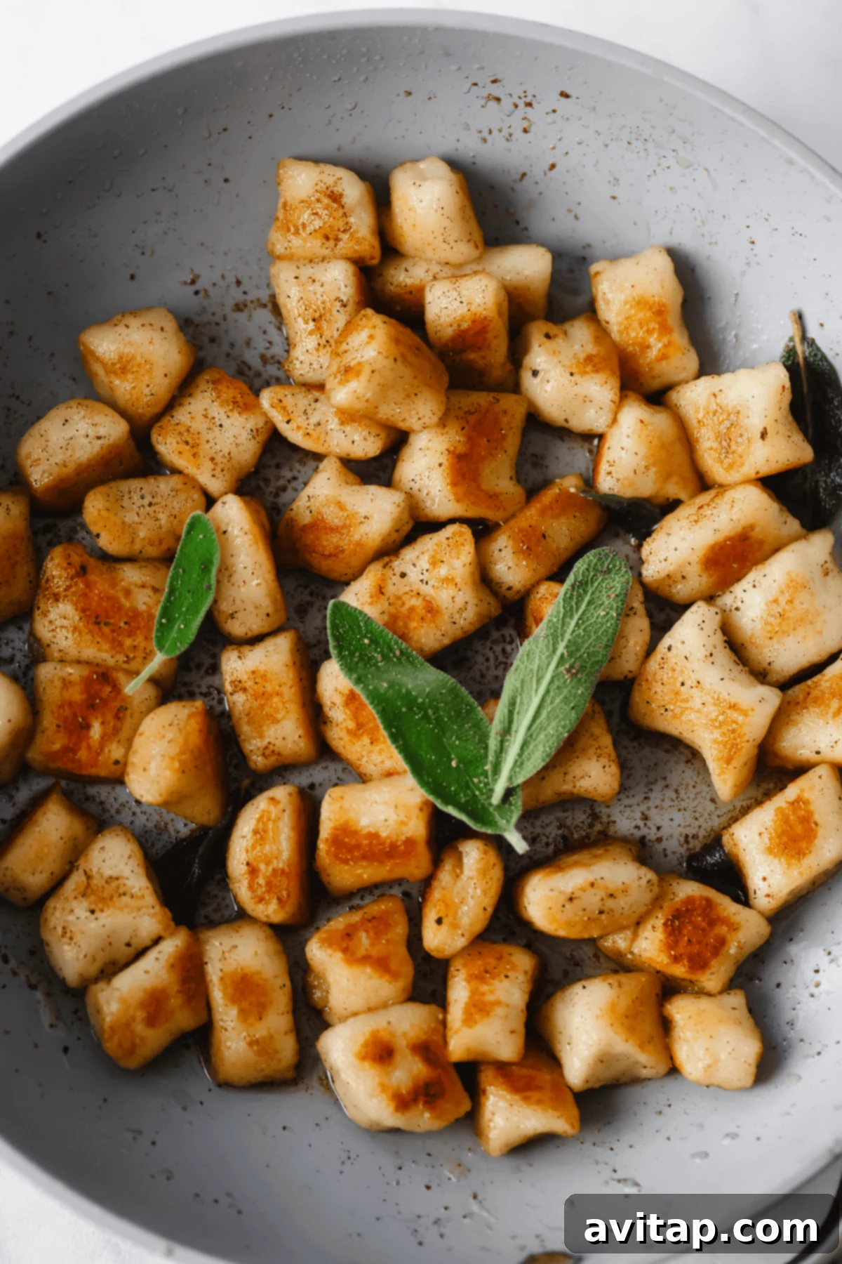 Pan-fried cottage cheese gnocchi with crispy edges, garnished with fresh sage leaves in a gray bowl.