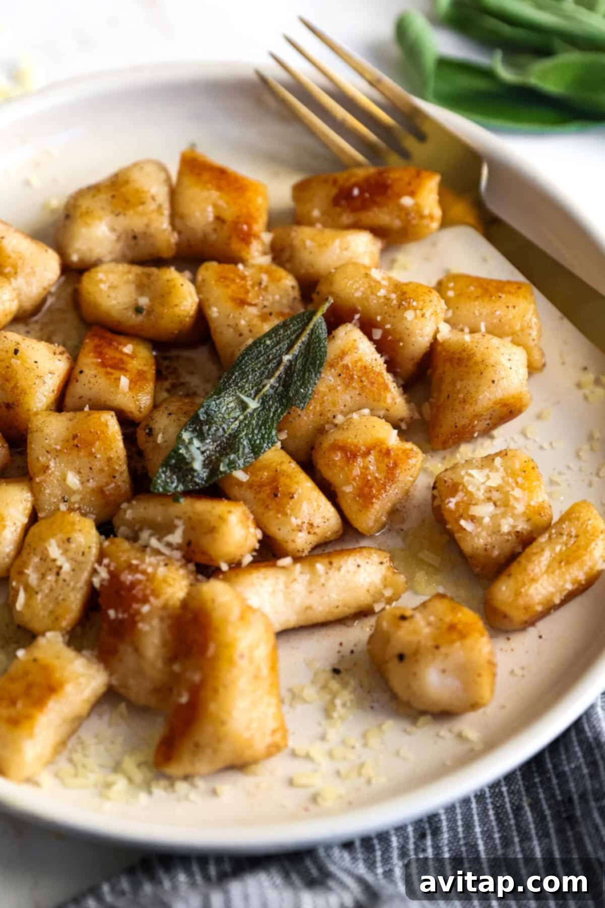 A plate of cottage cheese gnocchi topped with grated cheese and garnished with a sage leaf. A fork rests on the plate beside the gnocchi.