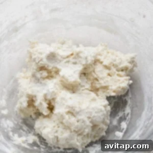A clear bowl containing a mixture of flour and butter, forming a crumbly dough.