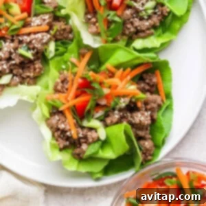 Vibrant lettuce wraps on a white plate, generously filled with seasoned ground beef, crisp sliced carrots, aromatic green onions, and toasted sesame seeds, with a small side bowl of carrots and red peppers for extra freshness.