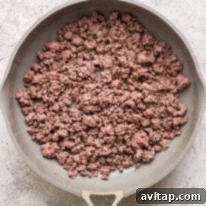 A frying pan containing cooked ground beef on a textured gray background.