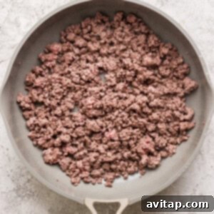 A frying pan containing cooked ground beef on a textured gray background.