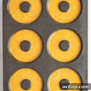 A six-cavity donut baking pan filled with pumpkin batter, ready for baking.
