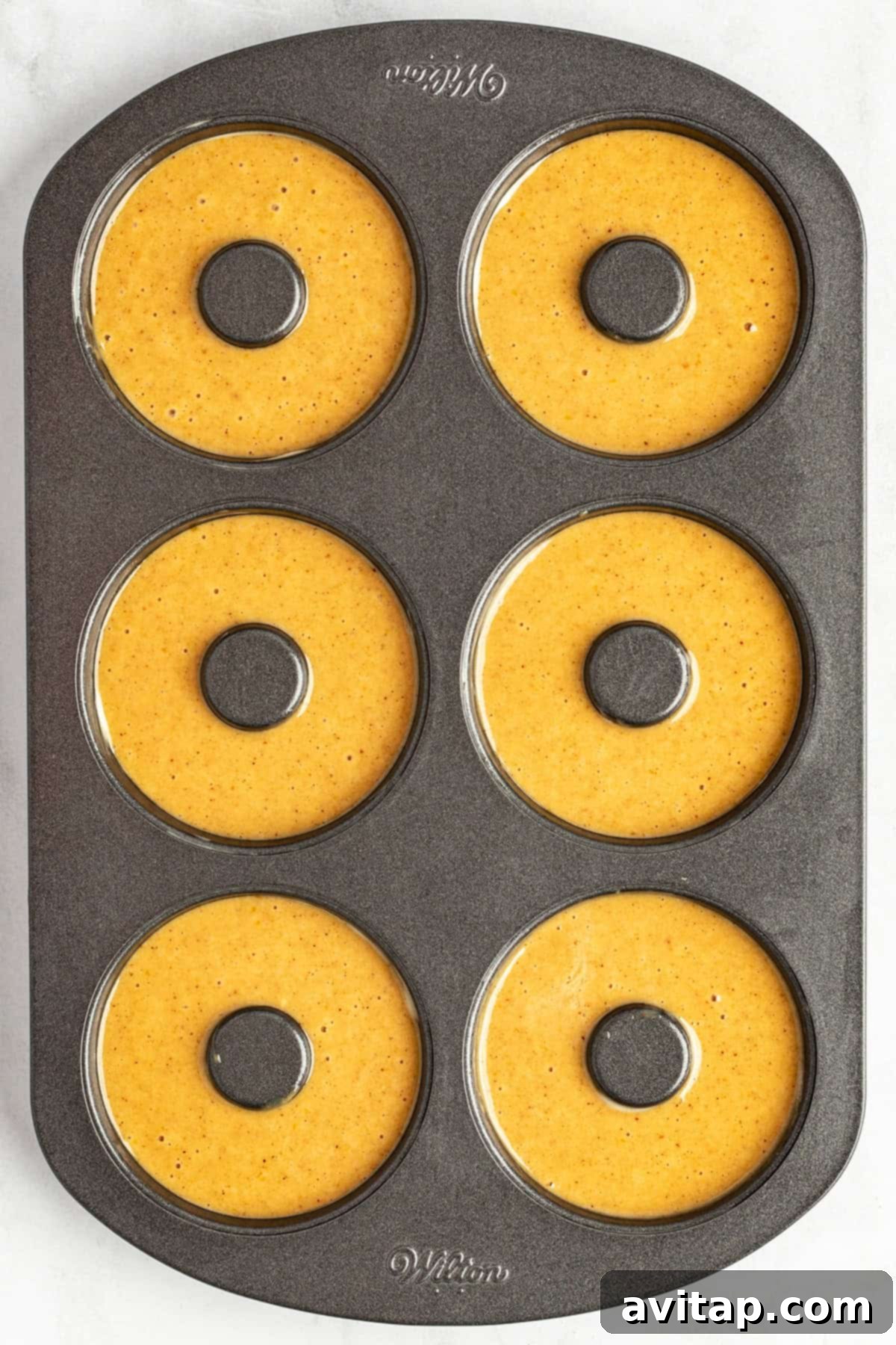 A six-cavity donut baking pan filled with pumpkin batter, ready for baking.