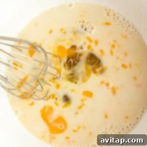 A whisk mixing eggs, milk, and oil in a white bowl.