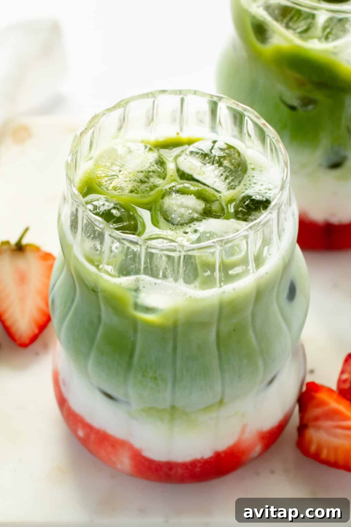 Strawberry Matcha Protein Refresher 2 A beautifully layered iced matcha latte with distinct green matcha, creamy white milk, and vibrant red strawberry syrup. Served in a clear, textured glass, garnished with fresh strawberry slices, and ready to be enjoyed.