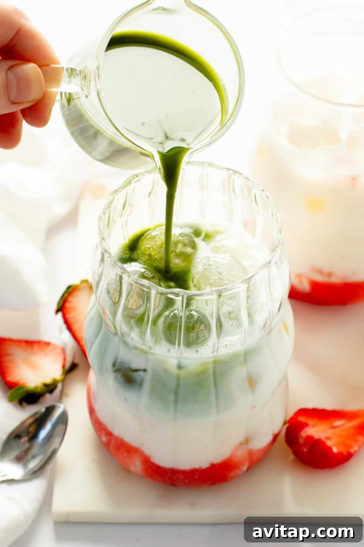 Strawberry Matcha Protein Refresher 5 A stream of creamy white milk being poured into a clear glass, which already contains a base of vibrant red strawberry puree and a layer of green matcha, demonstrating the layering process of the drink.