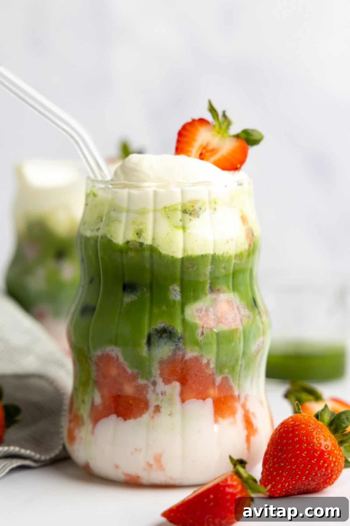 Strawberry Matcha Protein Refresher 6 A completed layered drink showcasing protein milk, vibrant green matcha, and red strawberry puree. It's elegantly topped with a swirl of whipped cream and a fresh strawberry slice, served in a clear glass with a transparent straw for a delightful presentation.