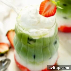 Strawberry Matcha Protein Refresher 7 A layered drink featuring protein milk, green matcha, vibrant fruit pieces, and whipped cream in a clear glass. It's elegantly topped with a strawberry slice and accompanied by a transparent straw.
