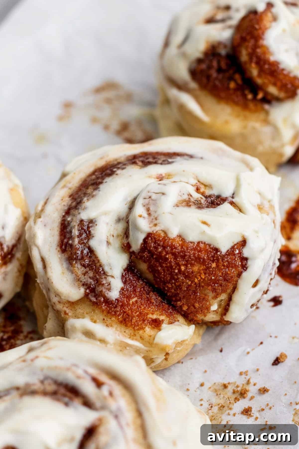 Protein-Rich Mini Cinnamon Rolls 2 Close-up of freshly baked small batch protein cinnamon rolls topped with creamy white icing on a parchment-lined baking sheet.