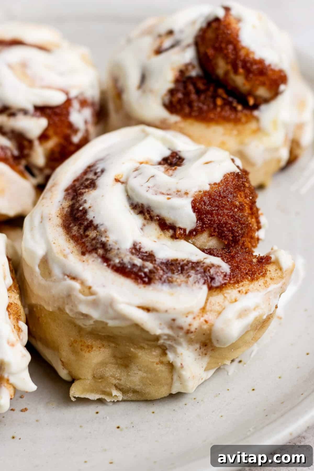 Protein-Rich Mini Cinnamon Rolls 5 Close-up of a single, perfectly baked cinnamon roll with smooth white frosting, presented on a simple white plate.