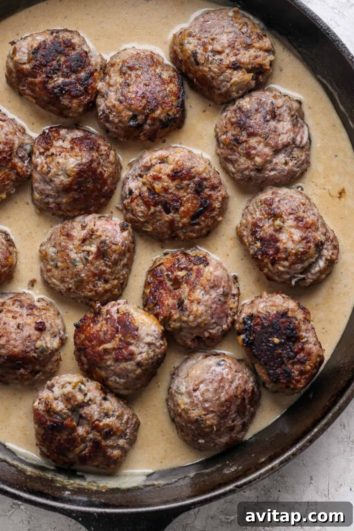 A skillet containing several browned meatballs in a creamy gravy.