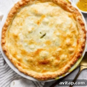 Curried Chicken Pot Pie 10 Golden brown pie with a flaky crust in a white dish, on a striped towel, with a spoon, fork, and a small bowl of spices nearby.
