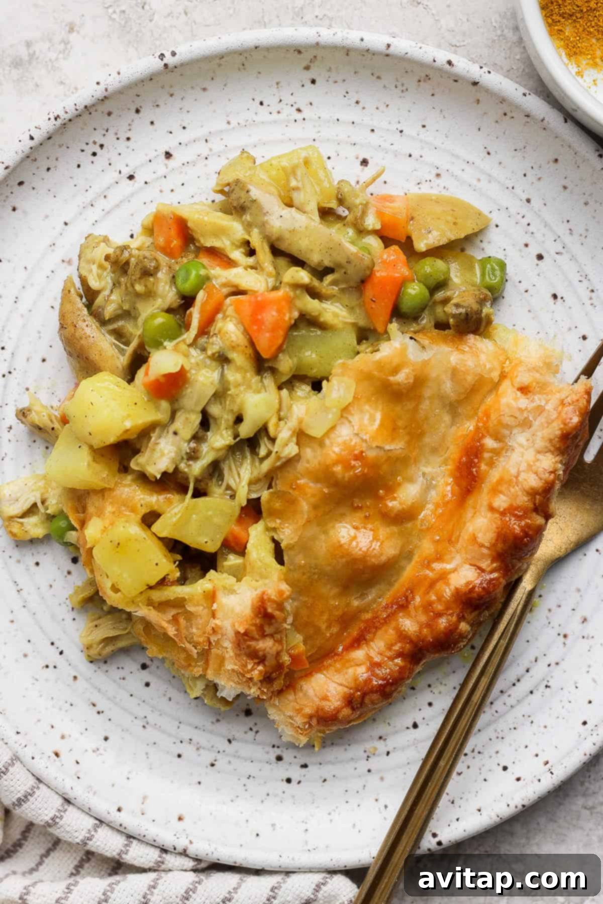 Curried Chicken Pot Pie 11 A slice of chicken pot pie with vegetables on a speckled plate, accompanied by a fork and a knife.