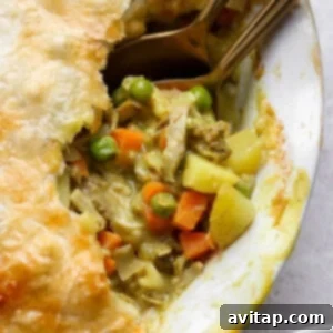 Curried Chicken Pot Pie 5 A close-up of a pot pie with a golden crust, showing a filling of chicken, peas, carrots, and potatoes, with two spoons partially inside.