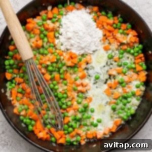 Curried Chicken Pot Pie 7 A skillet with sautéed carrots, peas, onions, butter, and a pile of flour, stirred with a whisk.