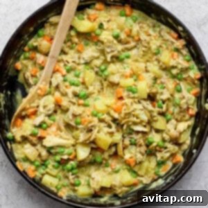 Curried Chicken Pot Pie 8 A skillet of cooked chicken, potatoes, carrots, and peas mixed in a creamy sauce, with a wooden spoon on the side.