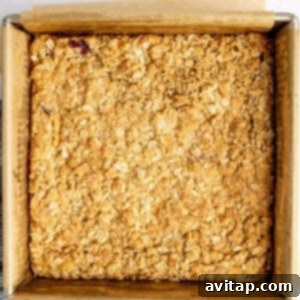 Square baking dish with a perfectly golden-brown baked oat crumble topping on parchment paper, resting on a light surface.
