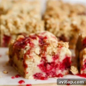 Close-up of crumbly dessert bars with a raspberry filling, topped with a drizzle of red sauce, arranged on parchment paper, ready to be served.
