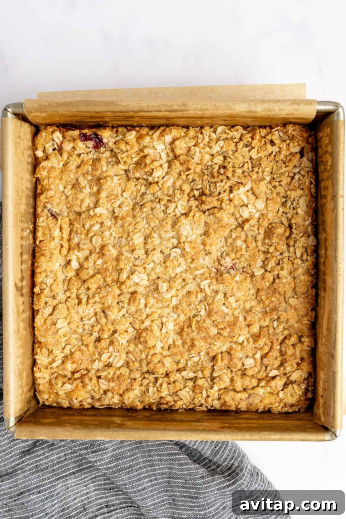 Square baking dish with a perfectly golden-brown baked oat crumble topping on parchment paper, resting on a light surface, ready to be enjoyed.