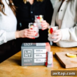 Three friends enjoying drinks, including a refreshing sleepy girl mocktail, sit beside a box of LMNT electrolyte drink mix on the wooden table.