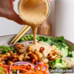 A hand carefully pouring creamy dressing over a vibrant salad mix, which includes shredded carrots, cucumber slices, red onions, crispy roasted chickpeas, and fresh green leafy vegetables, all in a large bowl.