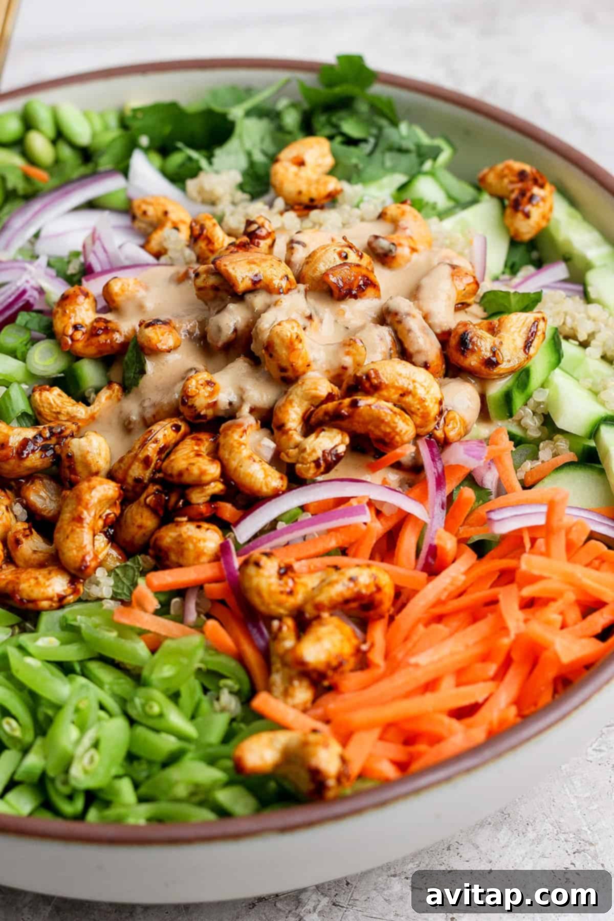 A beautifully arranged colorful salad, featuring toasted cashews, fluffy quinoa, crisp cucumbers, thinly sliced red onions, vibrant carrots, green beans, and mixed greens, all drizzled with a rich creamy dressing, served in an elegant bowl.
