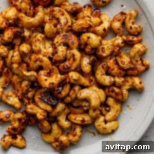 A plate of roasted cashews, generously seasoned with chili flakes and salt, resting on a clean light gray surface.