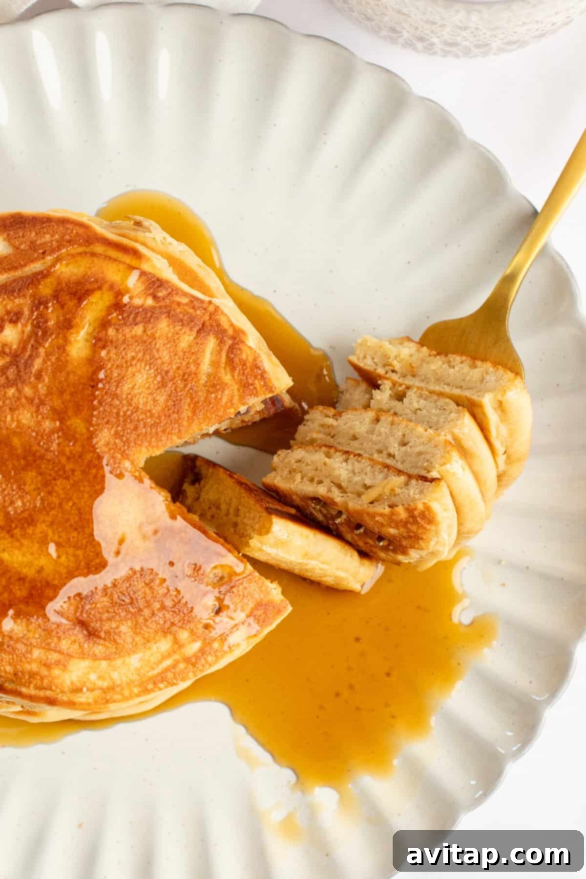 A partially eaten plate of golden-brown pancakes with syrup, showcasing their fluffy texture and inviting appearance. A fork holds a piece of a pancake, highlighting its deliciousness.
