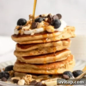 A stack of pancakes topped with blueberries, granola, yogurt, chocolate chips, and syrup being poured over them, representing the four flavor variations.