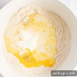A white bowl showcasing the pancake batter in progress, with a well in the center holding cracked eggs and creamy Greek yogurt, ready to be mixed with dry ingredients.
