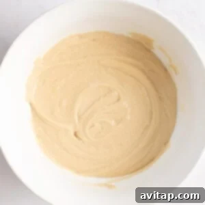 A white bowl containing smooth, light brown pancake batter on a light surface, illustrating the perfect consistency before cooking.