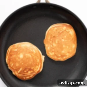 Two golden-brown protein pancakes sizzling gently in a black non-stick frying pan, showing the ideal cooking stage.