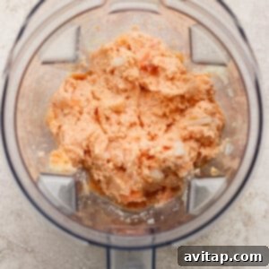 Sticky Sesame Ginger Salmon Meatballs 10 A blender containing a coarse, orange-colored mixture on a light textured surface.