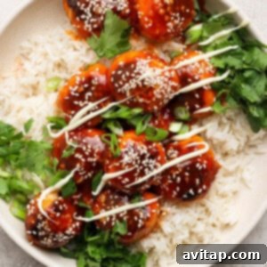 Sticky Sesame Ginger Salmon Meatballs 13 A plate of rice topped with glazed meatballs, sesame seeds, green onions, drizzled sauce, and fresh cilantro.