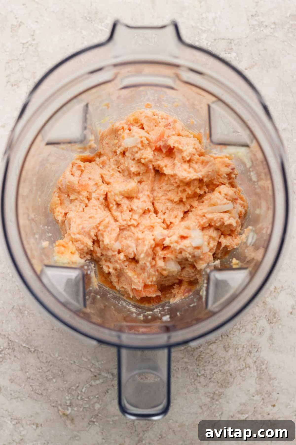 Sticky Sesame Ginger Salmon Meatballs 4 A blender containing a coarse, orange-colored mixture on a light textured surface.