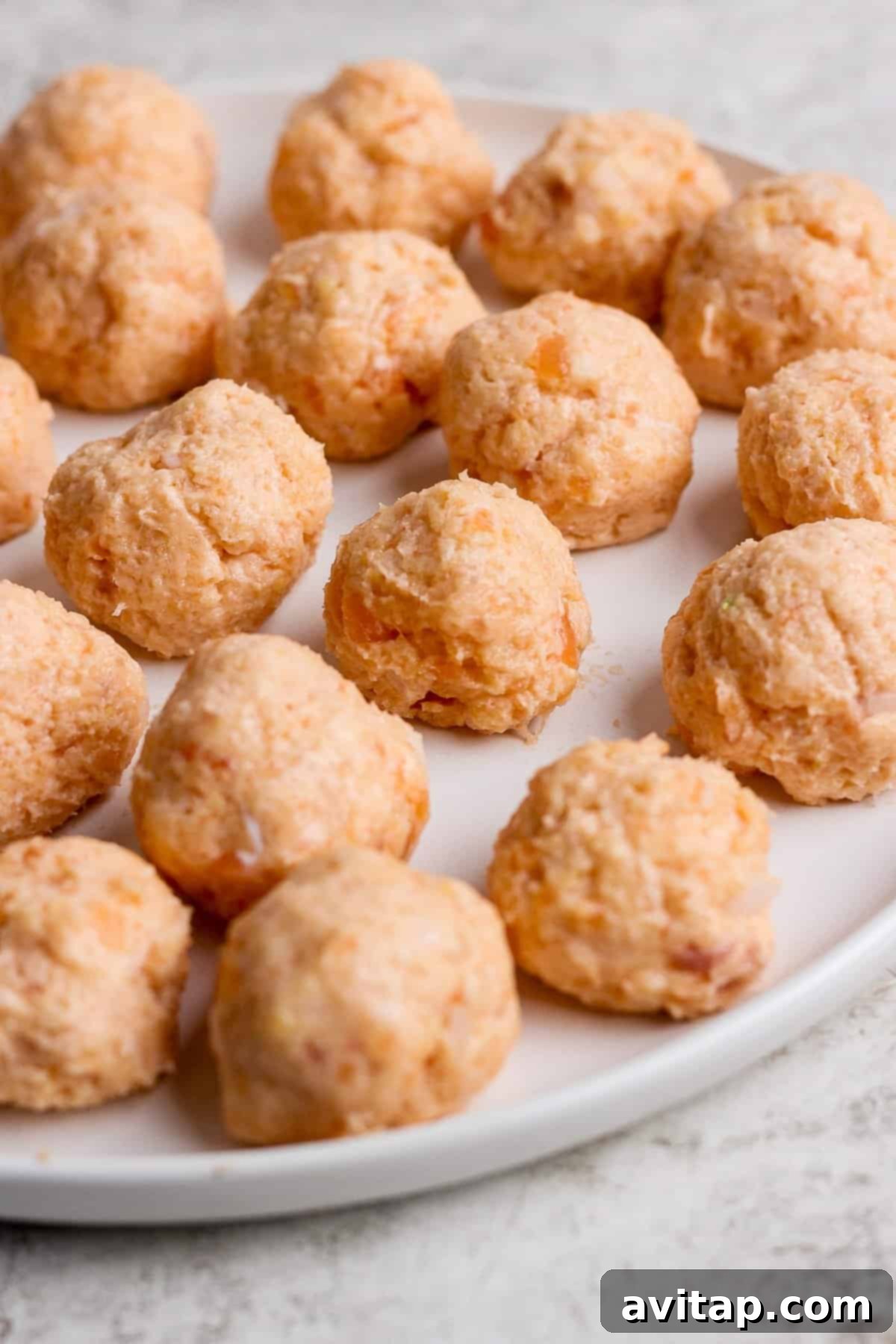 Sticky Sesame Ginger Salmon Meatballs 5 A plate of uncooked salmon balls arranged in rows on a white surface.