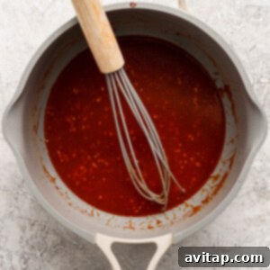 Sticky Sesame Ginger Salmon Meatballs 9 A whisk in a gray pan contains a thick red sauce with bits of seasoning.