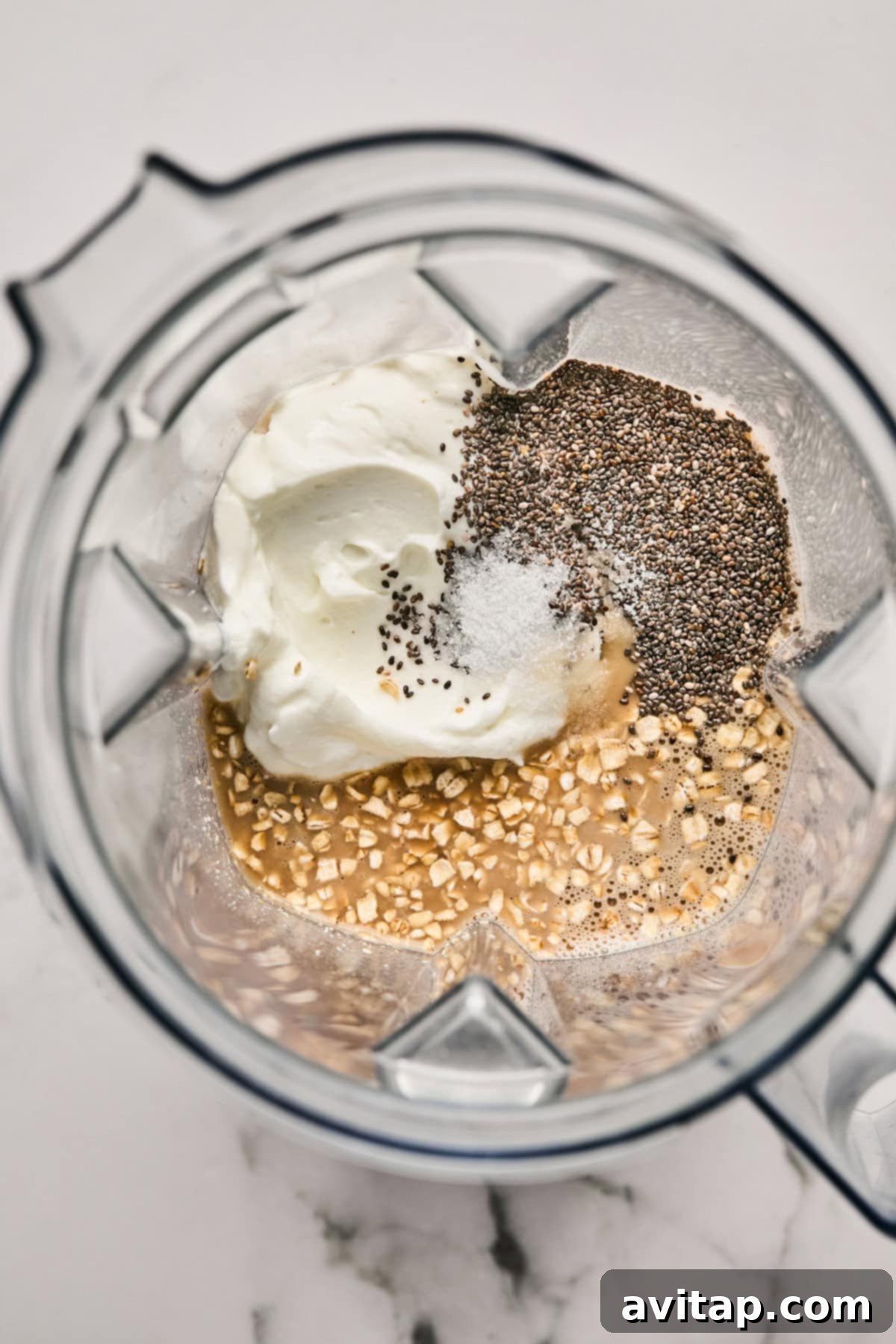Ingredients in a blender: yogurt, chia seeds, salt, oats, and a liquid mixture, ready for blending.
