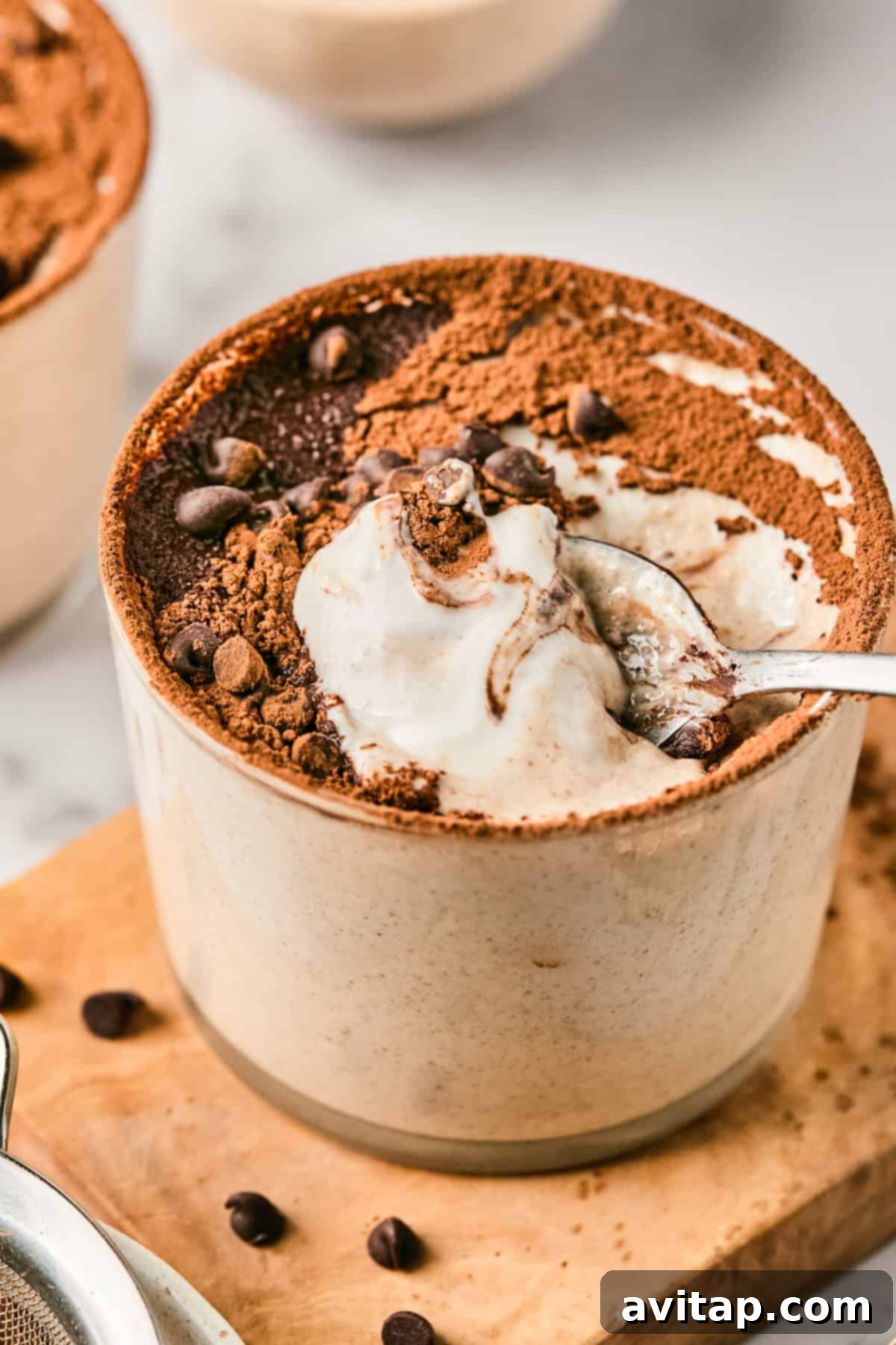 Tiramisu Blended Oats in a ceramic cup topped with cocoa powder and chocolate chips, with a spoon scooping a portion.