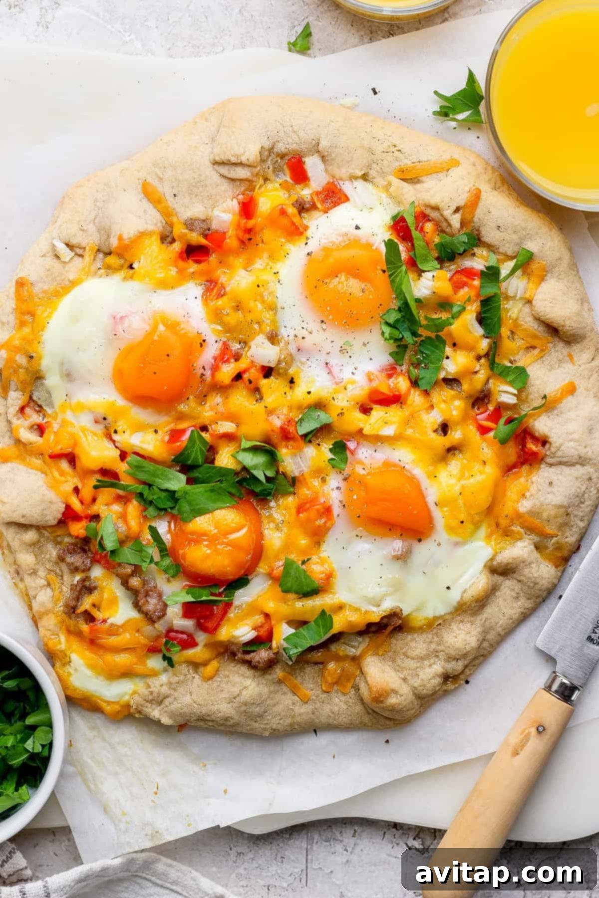 Hearty Morning Galette 2 A beautifully baked savory breakfast galette, topped with golden-yolked sunny-side-up eggs, melted cheese, vibrant red bell peppers, and fresh herbs, resting on parchment paper. A bowl of chopped parsley and a refreshing glass of orange juice are nearby, setting a perfect breakfast scene.