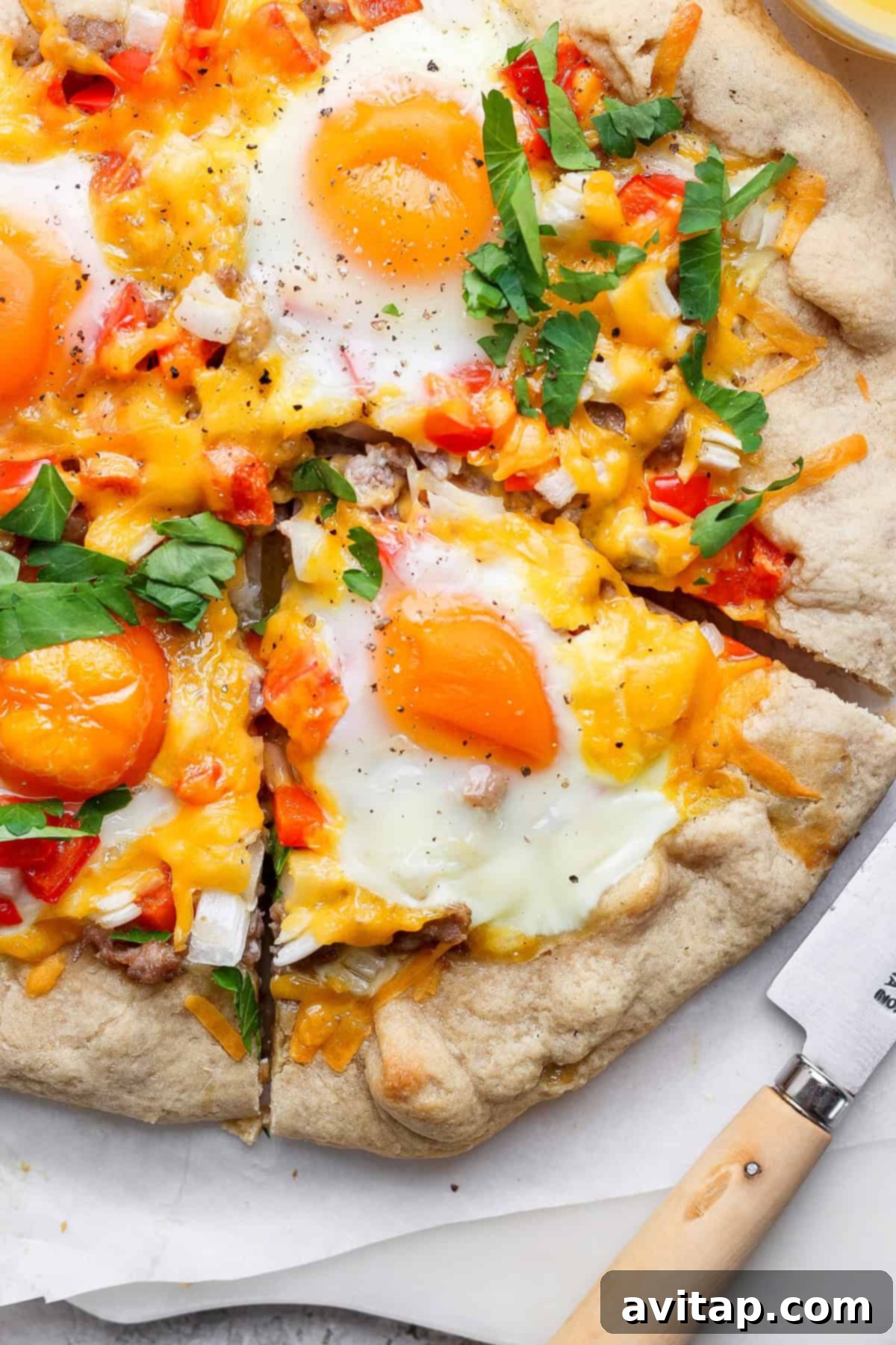 Hearty Morning Galette 4 A close-up view of a baked breakfast galette, featuring perfectly set sunny-side-up eggs, richly melted cheddar cheese, neatly diced red bell peppers and onions, and a sprinkle of fresh herbs. A single slice has been removed, with a knife resting artfully nearby, inviting you to indulge.